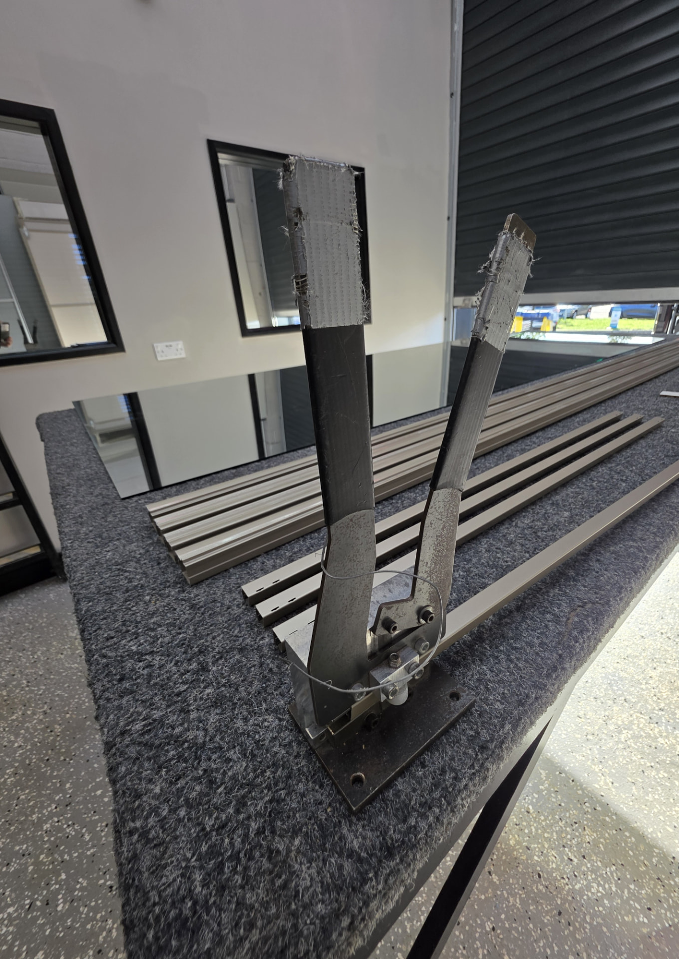 A frame press cutting an aluminium sliding door profile on the workbench, with finished door frames laid out in the Pontypridd workshop