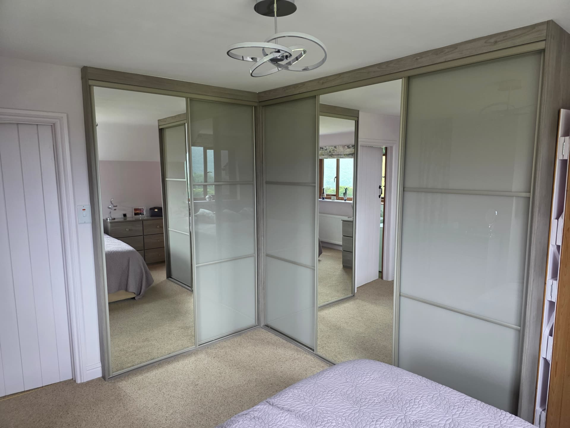 L-shaped corner wardrobe with pale coloured glass and full-height mirror sliding doors in a grey wood-effect surround in Carmarthen