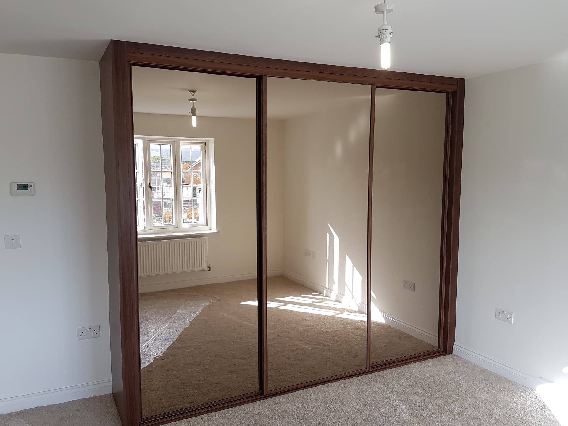 Three full-height mirror sliding doors in a walnut-effect frame and surround in Brynmawr