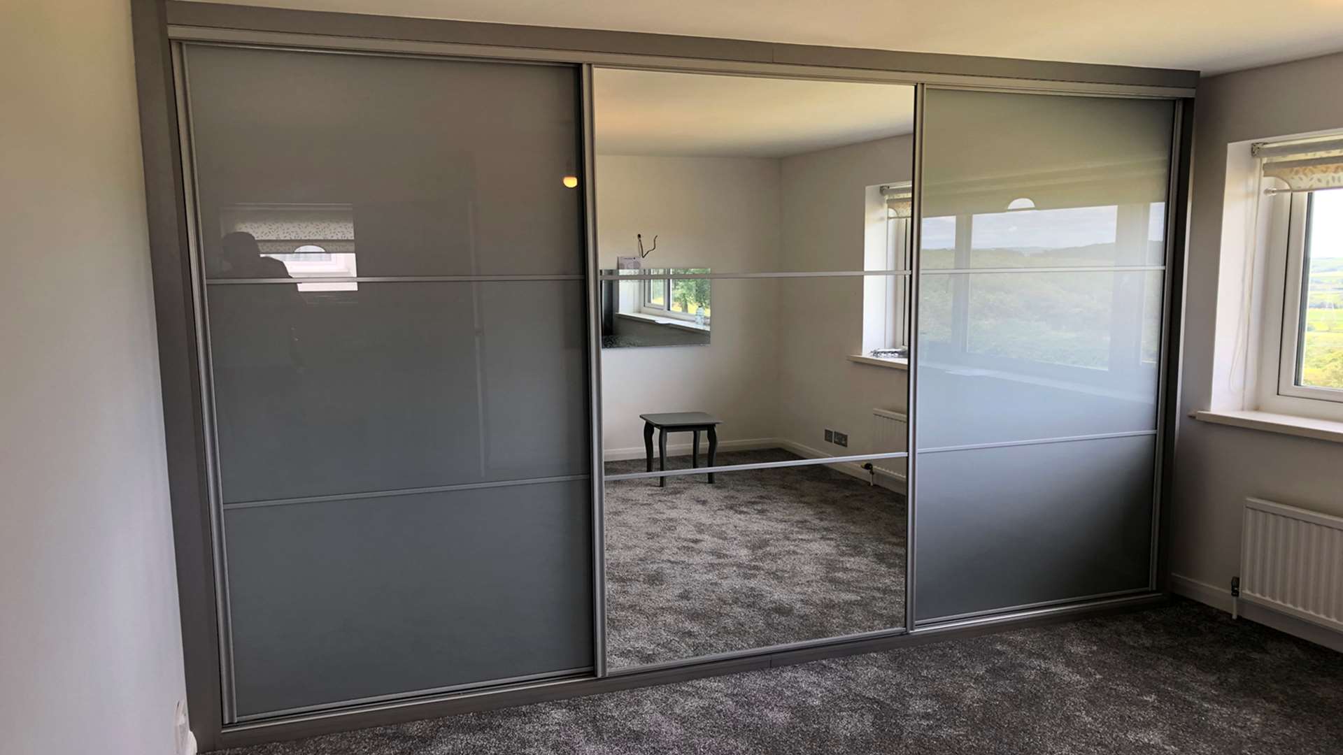 Three grey coloured glass and mirror sliding doors with silver frames and horizontal bars in Beaufort
