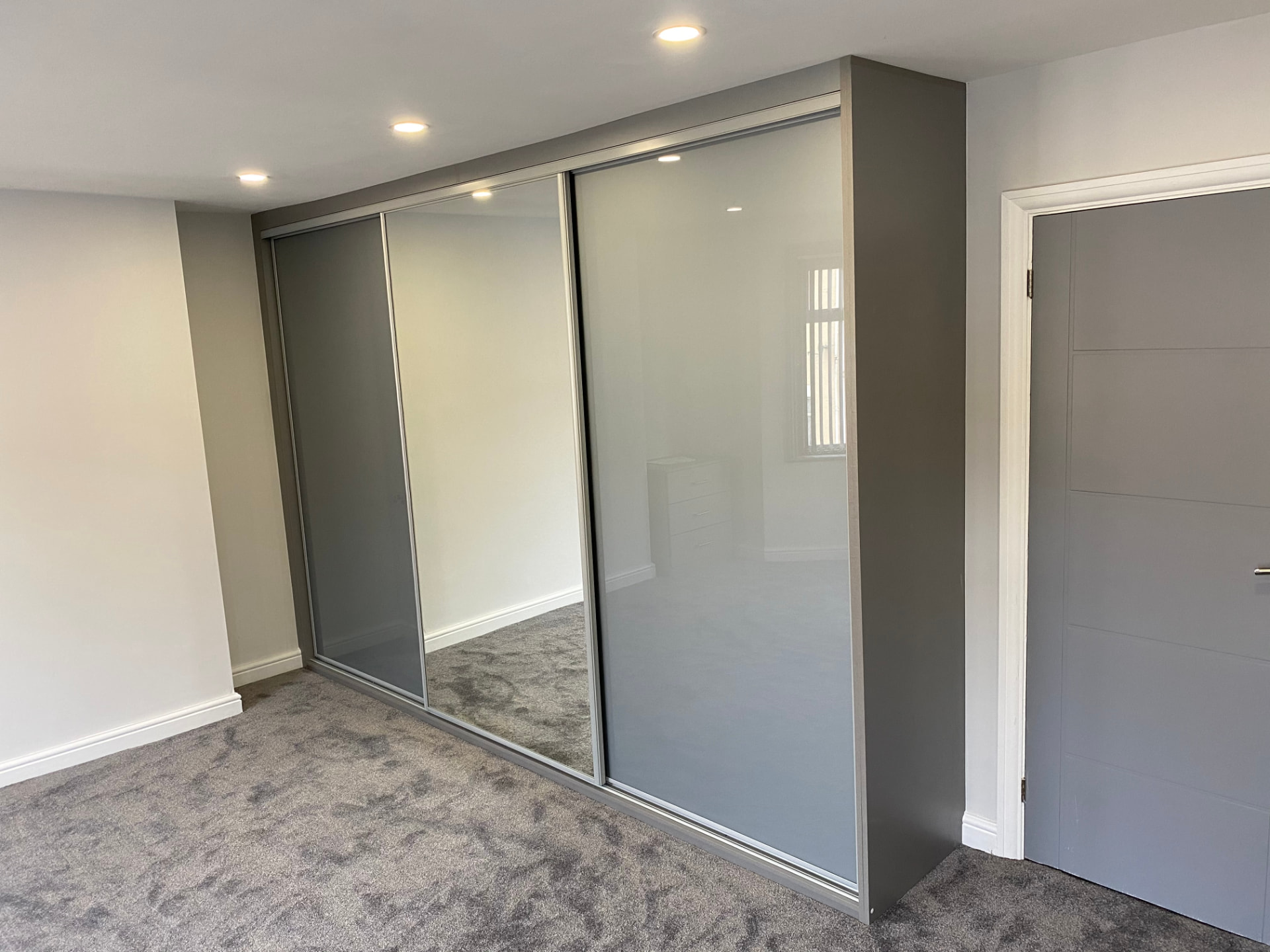 Three sliding doors with grey coloured glass either side of a full-height mirror, in a grey surround in Tredegar