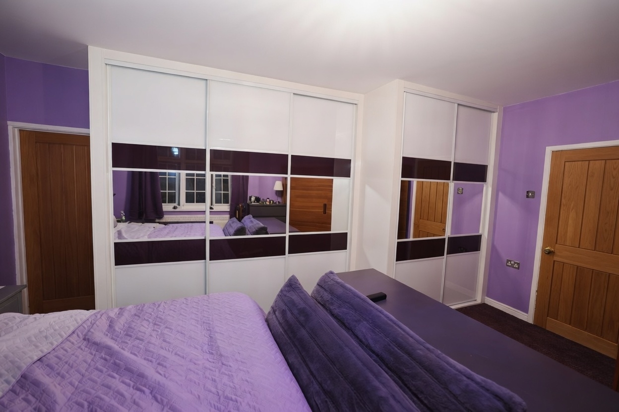 Corner run of white-framed sliding doors with white and deep purple coloured glass panels and wide mirror bands in Swansea