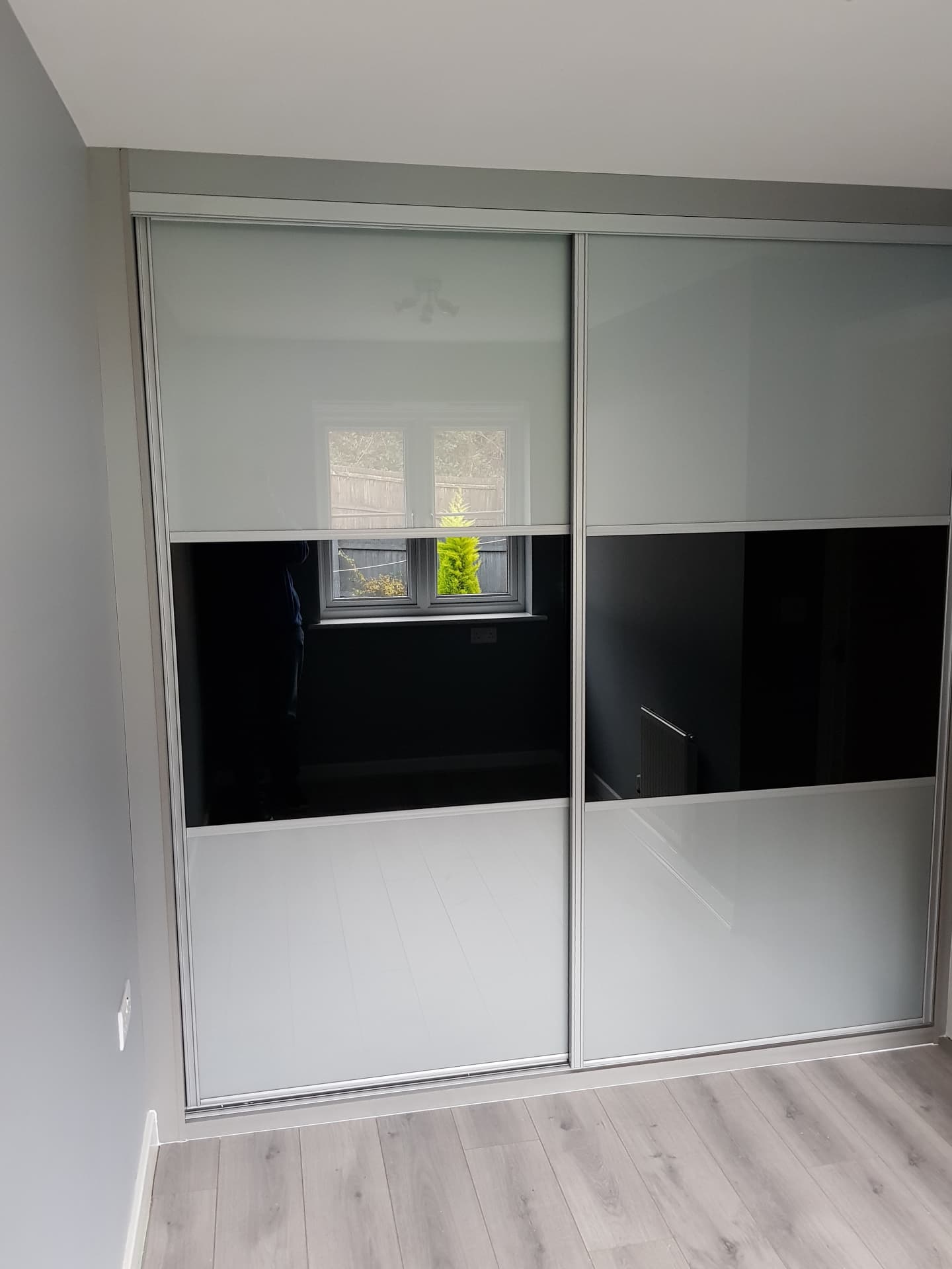 Two sliding doors in silver frames with white coloured glass above and below a black glass band in Ebbw Vale