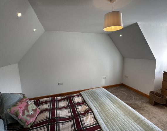 Loft bedroom with a sloping ceiling and an empty wall before fitted sliding wardrobes were installed