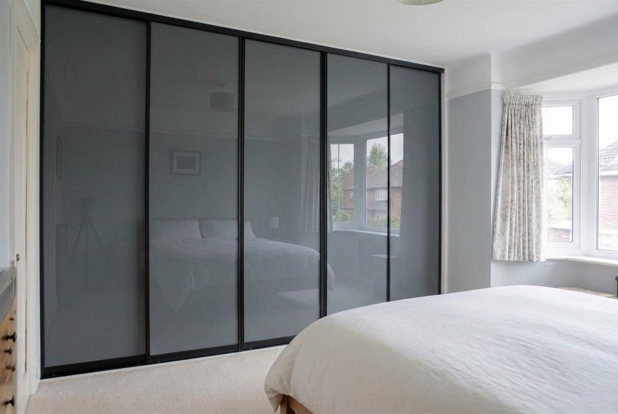 Smoked grey glass sliding wardrobe doors in slim black frames fitted floor to ceiling in a 1930s semi-detached bedroom in Newport